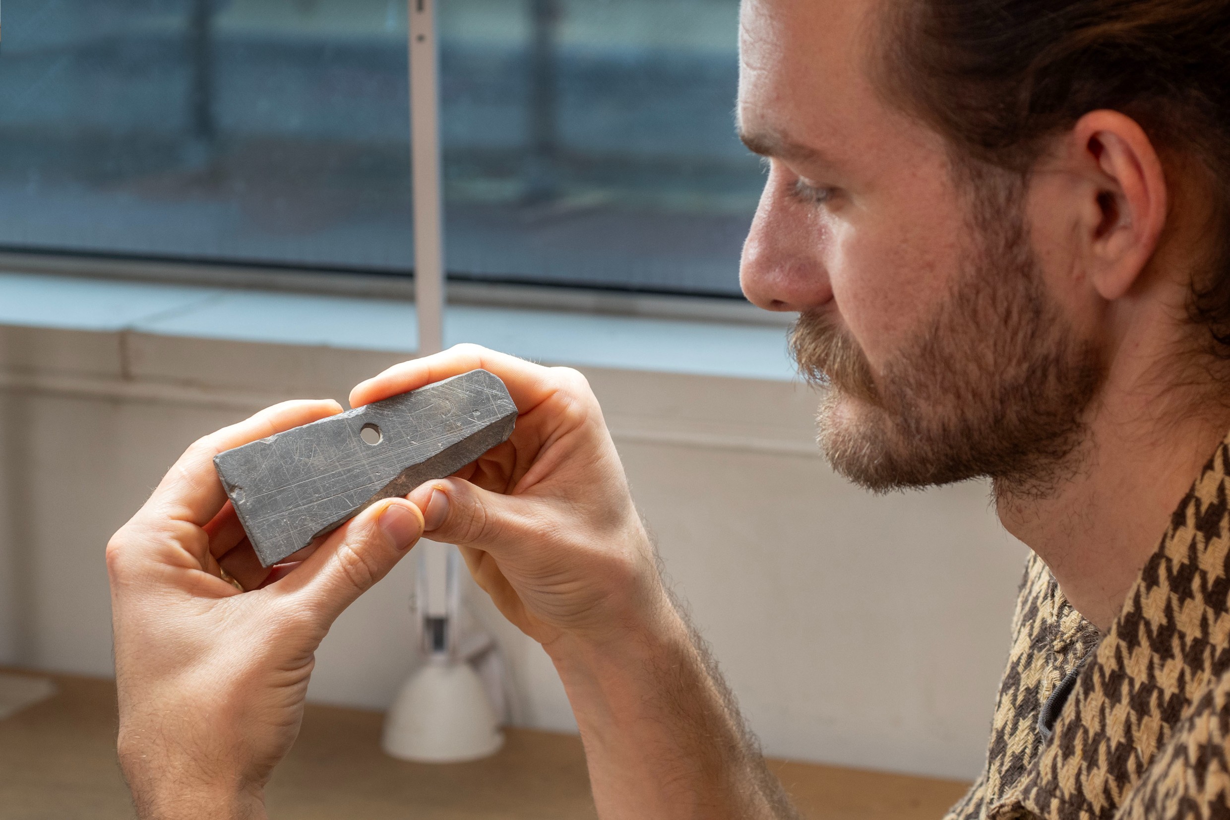 A man holding a rectangular piece of slate in his hands and looking at it, the slate has some faint scratches and marks
