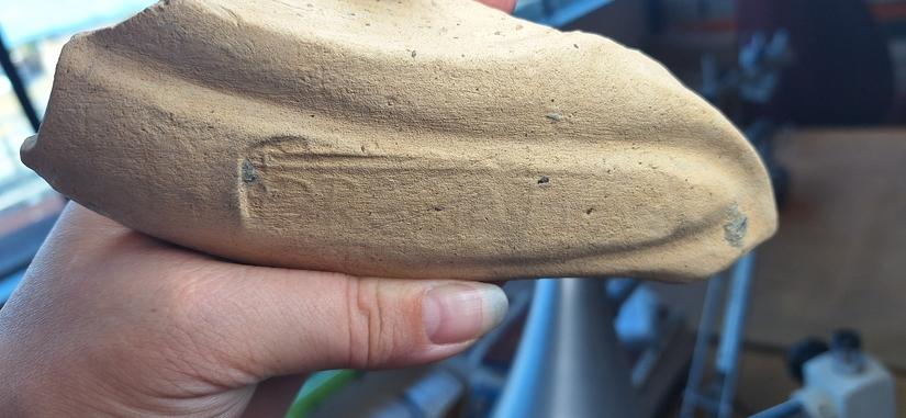 Hand holding the piece of mortaria with a faint stamp visible