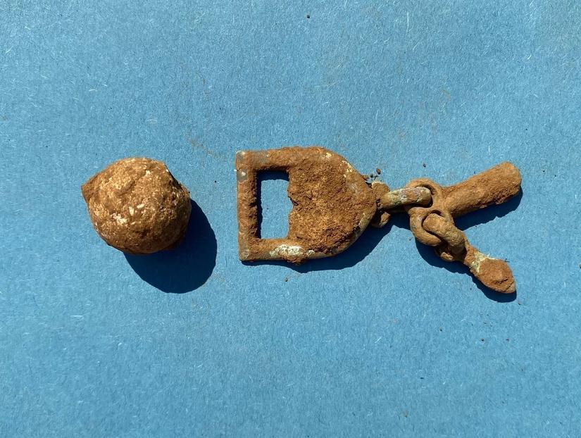 A metal musket ball and loop covered in dirt on a blue background