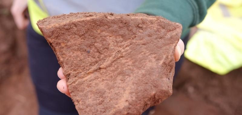 Archaeologist holding a curved piece of ceramic building material