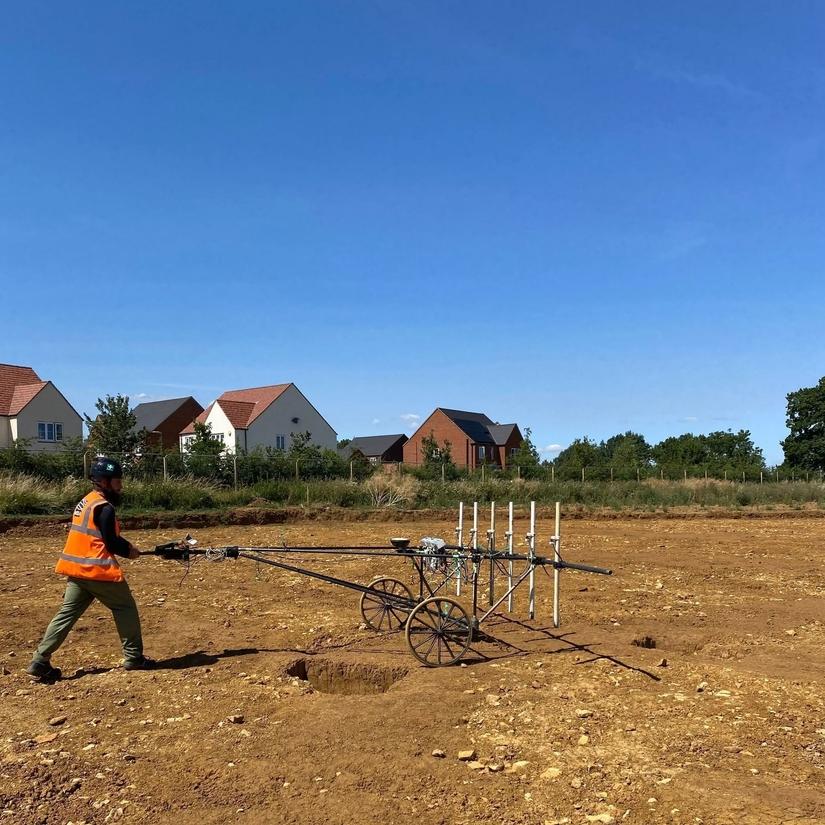 A member of the geophysics team pushing equipment across an excavated field