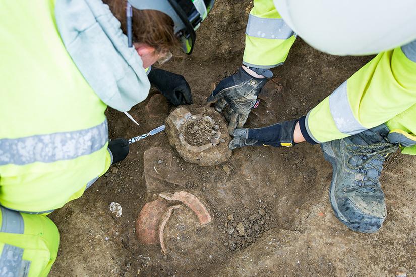 Two archaeologists in high vis PPE and hard hats excavated some pottery vessels