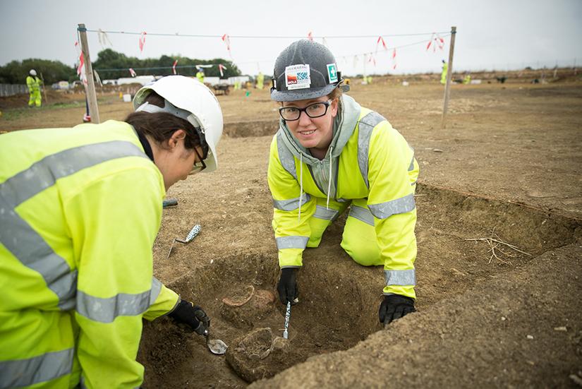 Supervisor Beth shows a volunteer how to excavate in a small trench