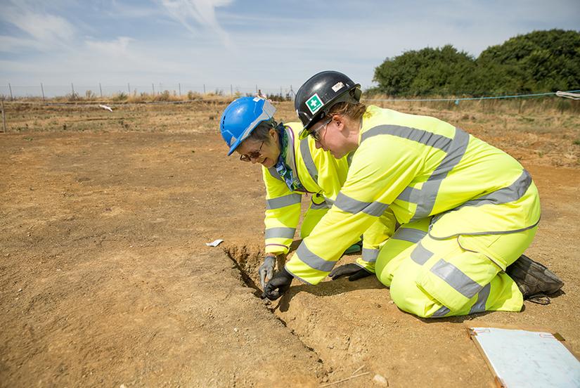Two women in high vis PPE and hard hats working on an archaeological excavation