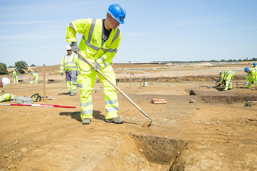 A man in high vis PPE excavating next to an archaeological trench