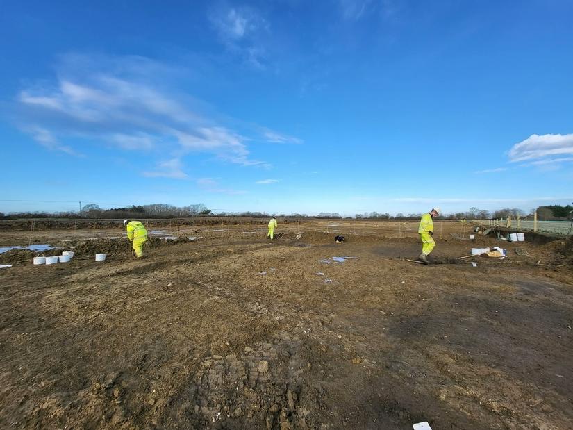 archaeologists excavating in a field. There is a dark circle - an unexcavated ditch