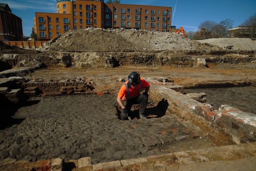 An archaeologist excavating the floor of a cellar which is covered with black soot