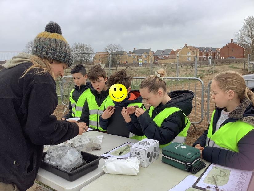 A group of children wearing high vis vests looking at pottery