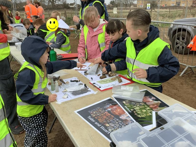 A group of children around a table sorting finds including pottery and tiny antique glass bottles into groups