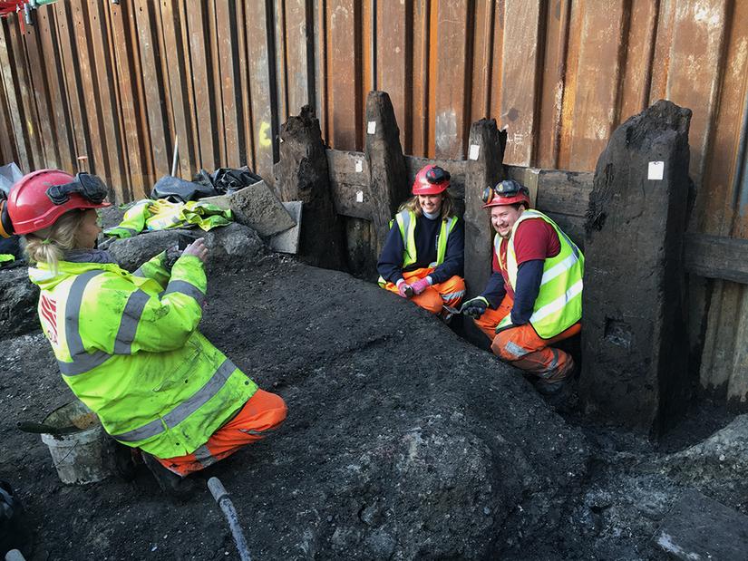 Two archaeologists being photographed by some preserved wood during an excavation
