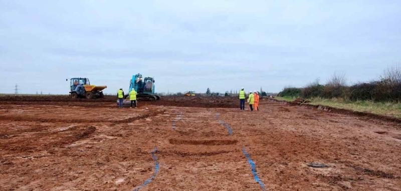 archaeologists watching a machine take the top soil off the site