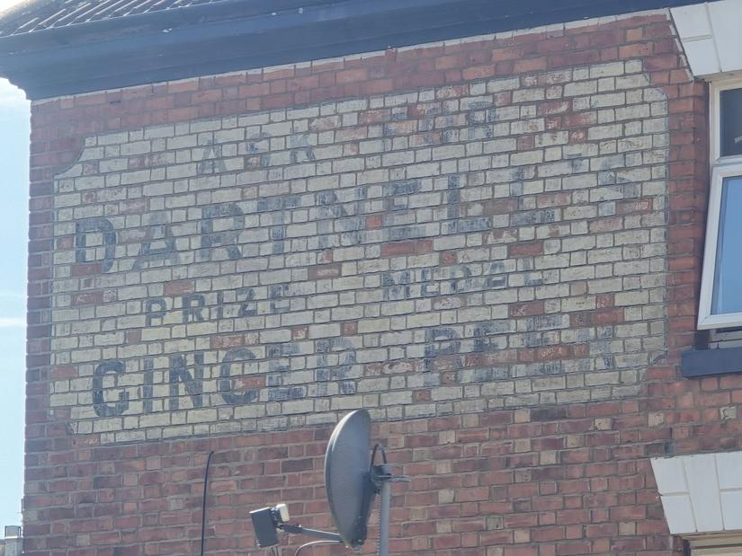 A painted sign on a wall. It is faded but the text can still be read. It says "Ask for Dartnell's prize medal ginger beer"