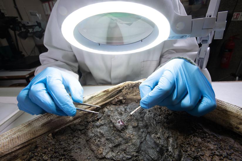 Photo of conservator cleaning the delicate cross under a microscope, using a cotton bud and tweezers