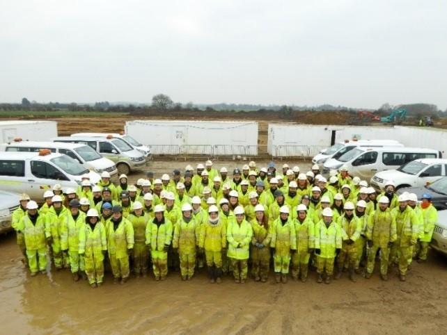 A large group of archaeologists posing for a group photograph, they are all wearing high vis PPE