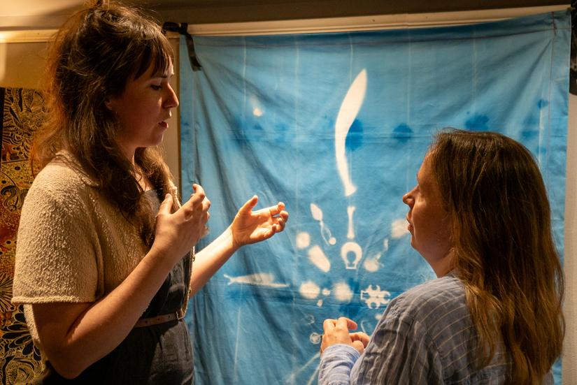 Two people talk in front of a piece of cynotype art