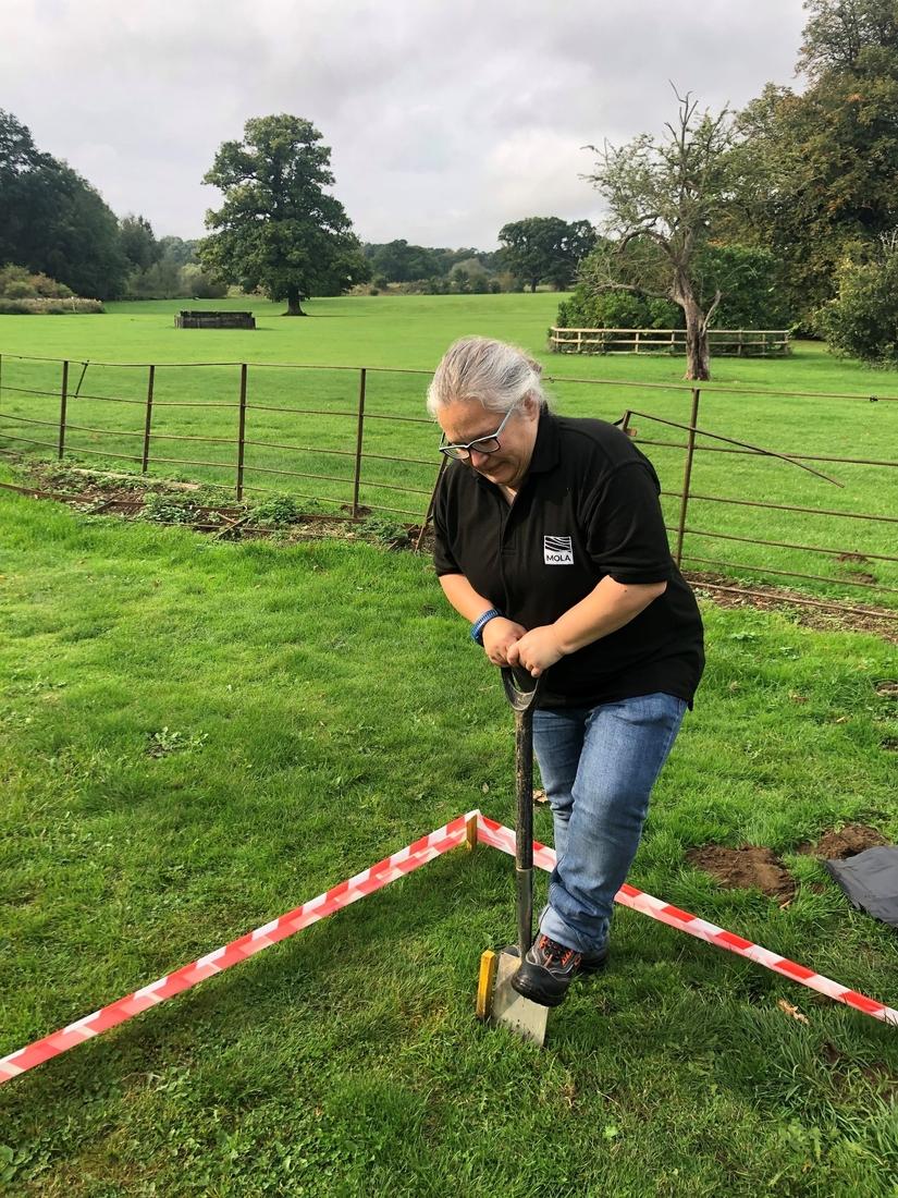 Photo of archaeologist digging into the grass with a spade