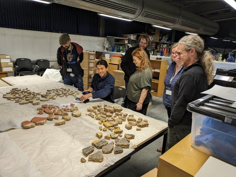 A group of people gathered around a large table in an office. On the table are lots of small pieces of decorated wall plaster
