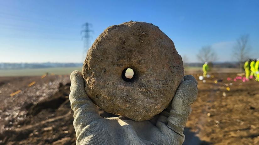 A small, stone coloured, donut shaped object being held by an archaeologist.