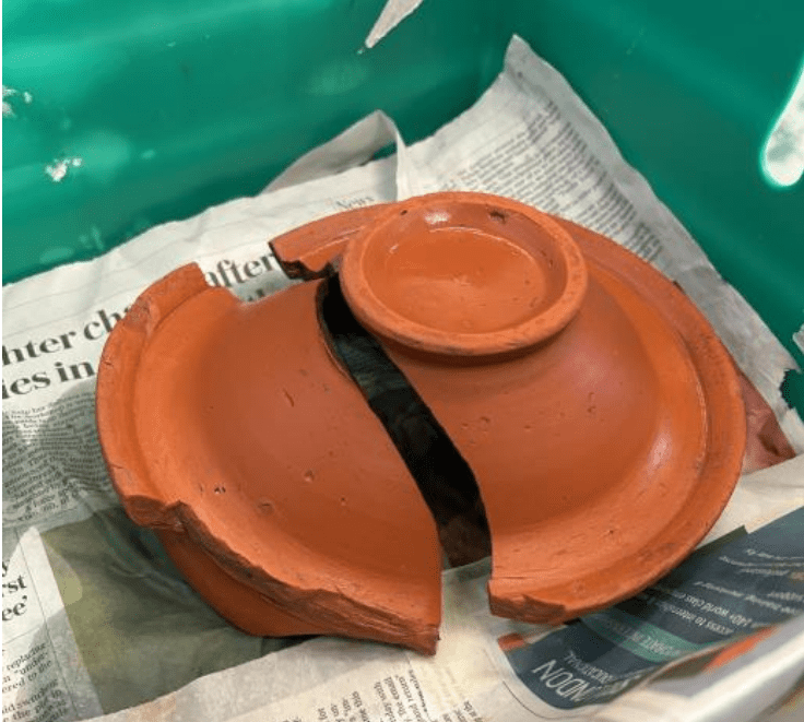 An upturned bright orange bowl (Samian Ware), broken in two pieces.