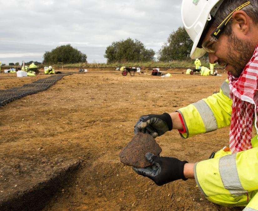 An archaeologist on an excavation site holding a large piece of decorated pottery