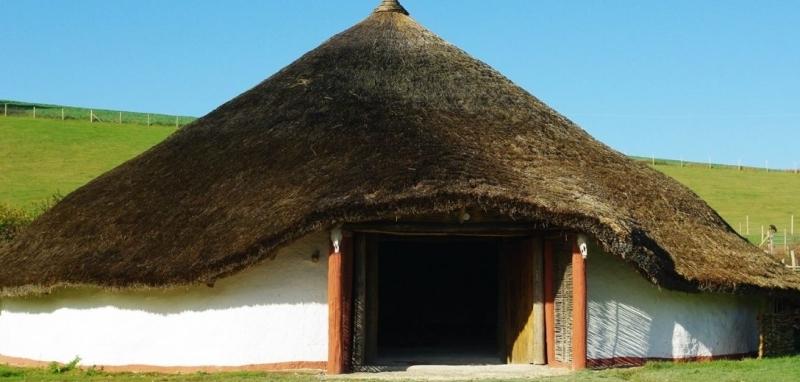 Photo of roundhouse, with low walls and thatch roof