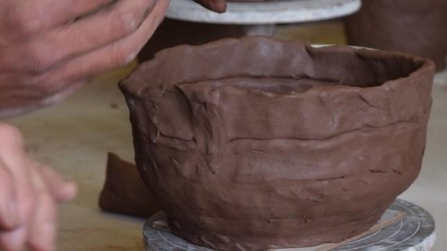 Potter smoothing out a coiled pot on a wheel