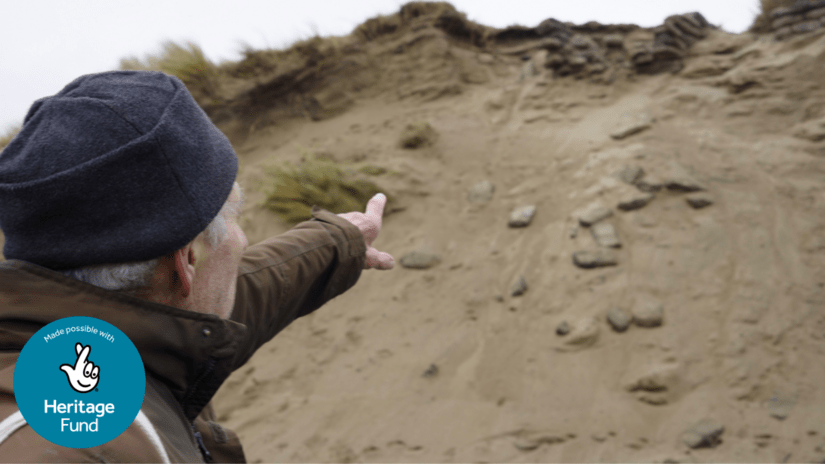A person pointing at a sandbank with sandbags eroding out