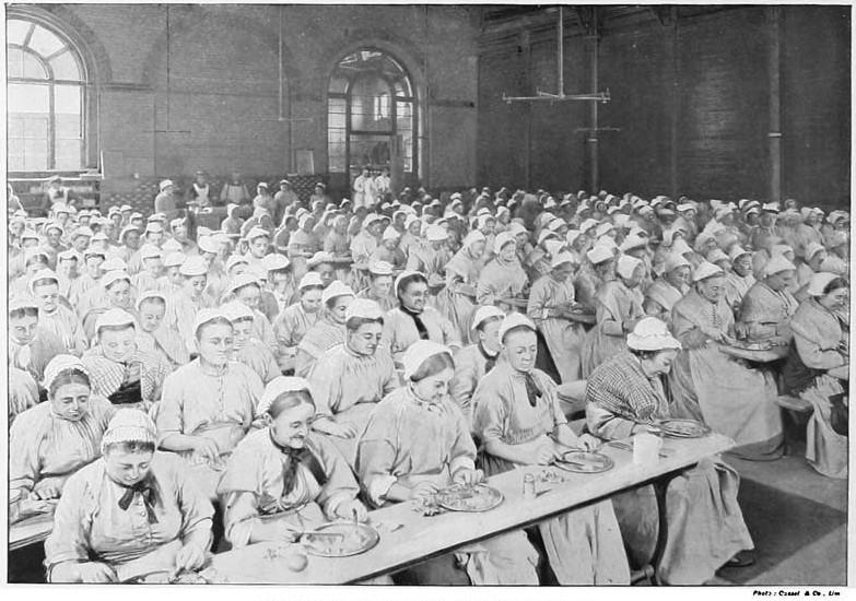 Black and white historic photo of a large number of women in victorian dress eating in a dining hall