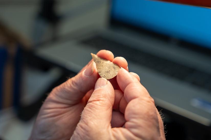 two hands holding a small tear shaped flint arrowhead