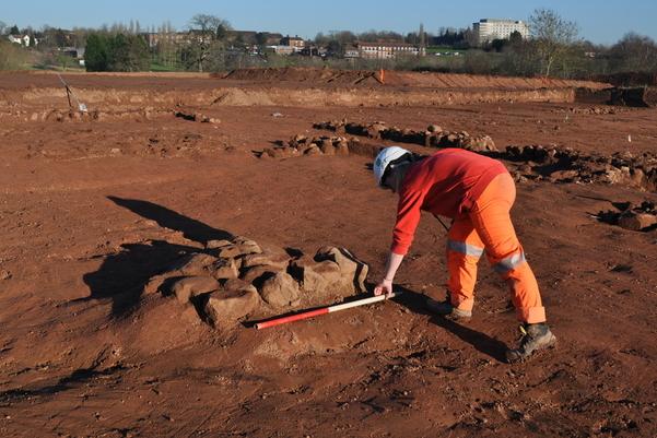 Archaeologist laying out a scale bar in front of a feature