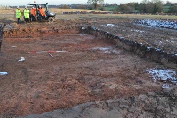 Archaeologists standing by a large trench