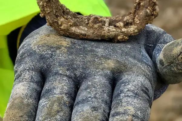 gloved hand holding a corroded metal object shaped like a horseshoe