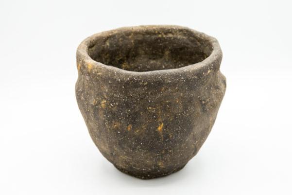 A complete dark clay pot with white speckles