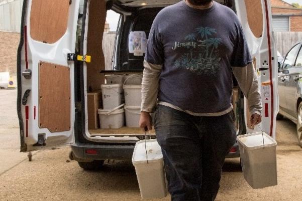 A man carrying two sample buckets from a van