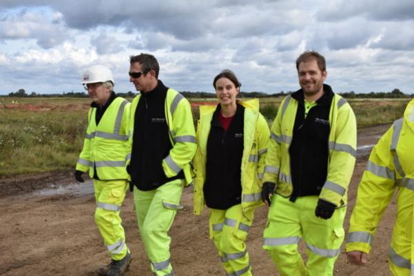 A group of four archaeologists wearing yellow PPE over black fleeces. Emma is a woman with dark hair in the middle of the group. she is looking at the camera.