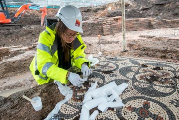 A woman in PPE and a hard hat conserving a Roman mosaic on site