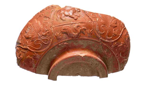 A large fragment of a decorated bowl. It is an orange-red colour and covered in designs of animals and leaves