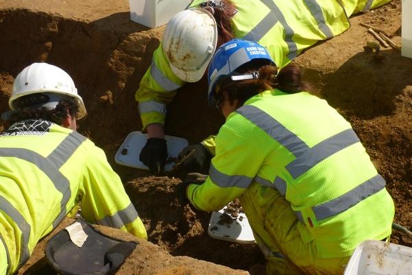 three archaeologists excavating in a trench