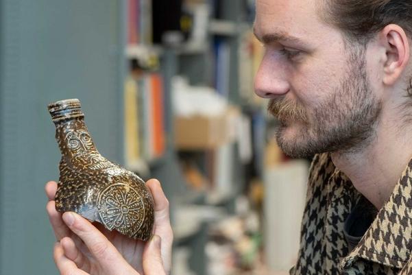 An archaeologist holding a large section of a jug with a face on the front