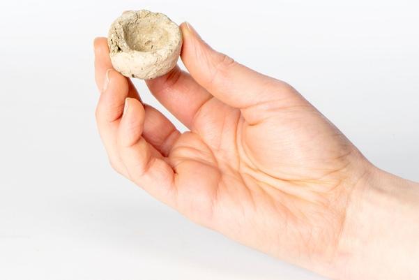 hand holding a tiny iron age pot between two fingers