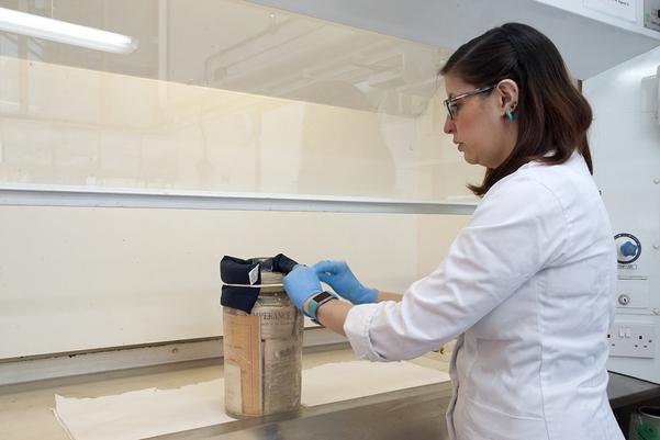 A woman in a white coat opens a glass bottle with papers inside