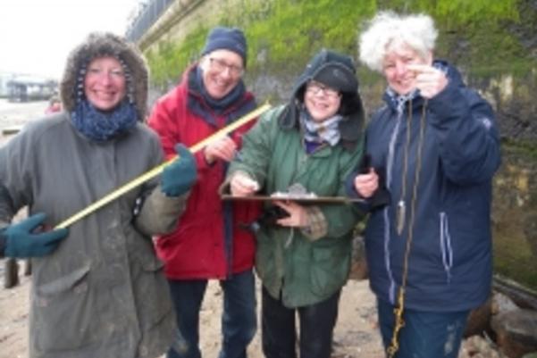 Photo of volunteers posing with their tools, a tape measure, plumb line and clipboard
