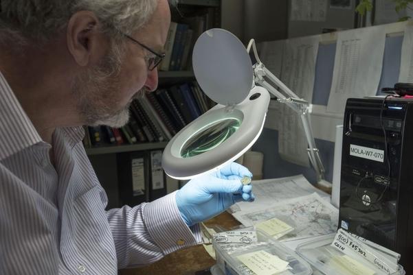 an archaeologist looking at a small find through a magnifier