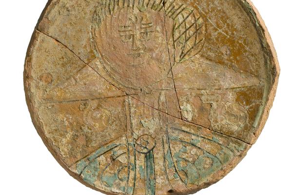 A circular pale brown plate decorated with the image of a woman. The neck of her dress has a very large collar.