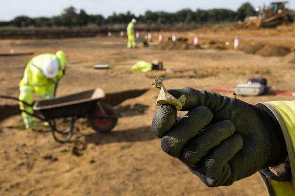 An archaeologists holding a chicken shaped brooch