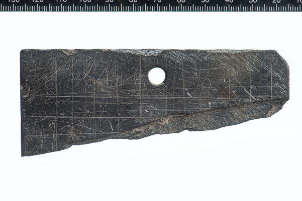 The top corner of a tablet with lines draw across it and some letters written on it.