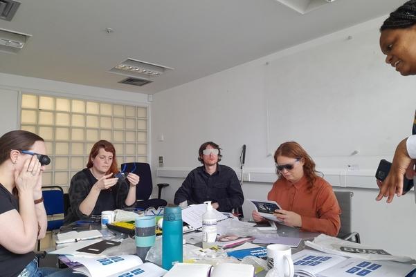 A group of people sitting around a table trying on different types of glasses.
