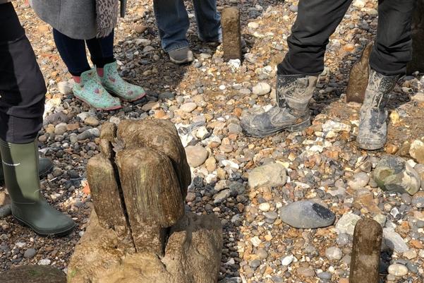 A group of people standing around a wooden object on the foreshore
