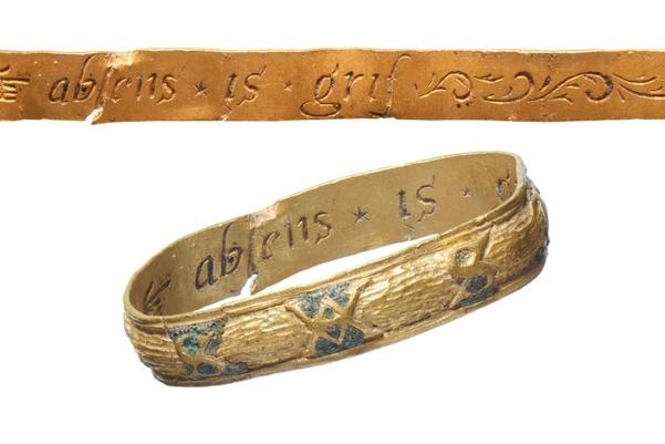 A gold ring with writing on the inside of the band. The outside is decorated with flowers.
